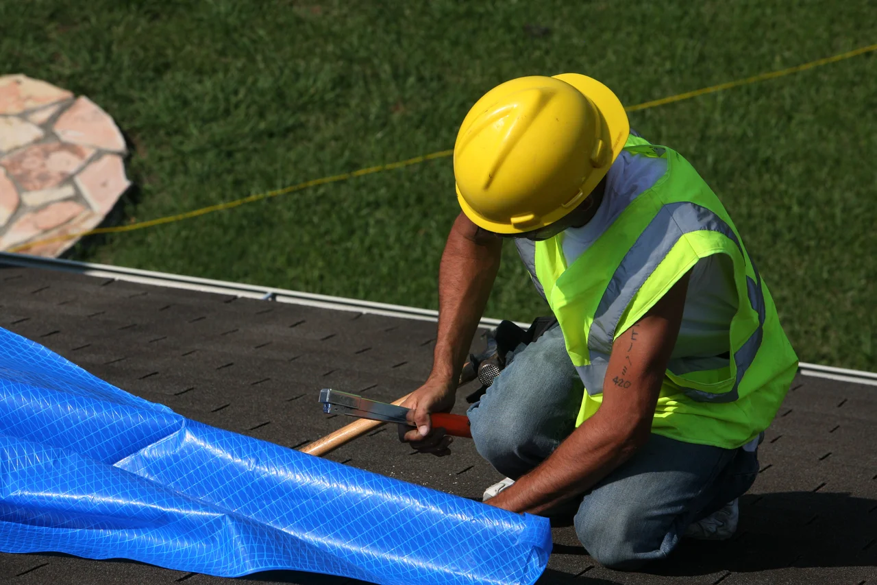 Worker installing a blue temporary covering on a roof